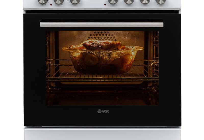 VOX electric oven with glass door roasting chicken inside, black and white stove design, control knobs on top